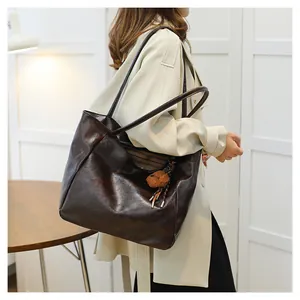 Dettaglio della borsa tote in pelle marrone scuro con logo e ciondolo a orsetto