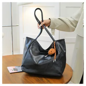 Dettaglio borsa tote in pelle nera con logo impresso e ciondolo a forma di orsetto bruno