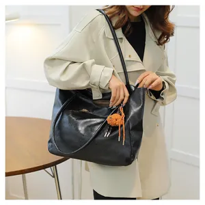 Dettaglio di una borsa tote nera in pelle con ciondolo a orsetto su trench beige