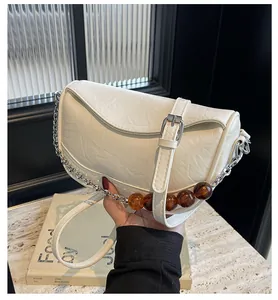 Detalle del bolso nube plisado blanco con cadena plateada y cuentas de color marrón oscuro