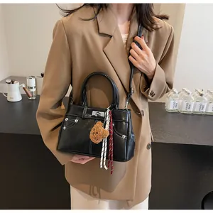 Sac style Kelly noir mat porté en bandoulière avec un pendentif d'ours en peluche mignon