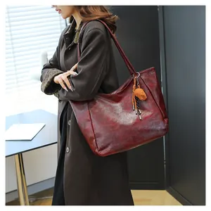 Dettaglio della borsa tote bordeaux vintage con texture in pelle oleosa e ciondolo