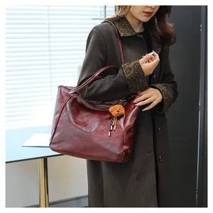 Dettaglio della borsa tote in pelle bordeaux con ciondolo a orsetto e logo impresso