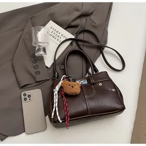Détail du sac Kelly marron avec coutures contrastées, fermoir en métal et charm d'ours