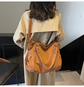 Sac hobo en cuir mat marron avec détails de rivets porté à l'épaule par un mannequin