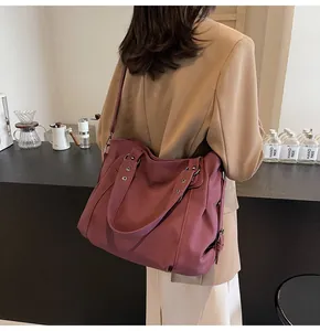 Détail d'un grand sac cabas bordeaux porté à l'épaule dans un décor de café cosy