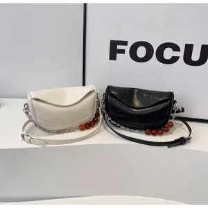 Detalle de bolsos de media luna crema y negros con cuentas de ámbar y cadena plateada