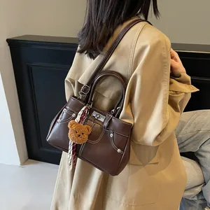 Sac Kelly marron foncé avec surpiqûres blanches et breloque ours sur trench-coat kaki