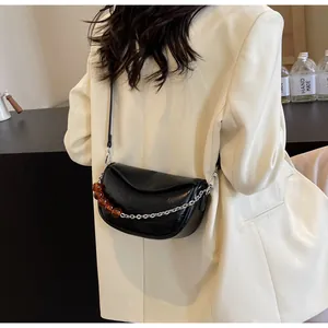 Detalle del bolso nube negro con cadena plateada y cuentas ámbar sobre un blazer beige