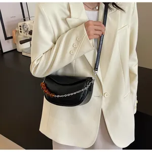 Detalle de un bolso de media luna negro brillante con cadena plateada y cuentas en modelo