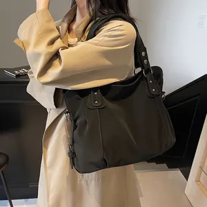 Grand sac cabas noir minimaliste avec rivets argentés porté par un mannequin en trench