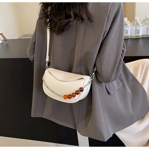 Detalle de bolso medialuna blanco con cadena plateada y cuentas de resina ámbar