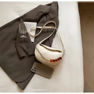 Detalle del bolso nube crema con cadena de ámbar sobre una americana marrón