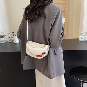 Bolso bandolera blanco minimalista con cuentas de ámbar y cadena plateada en una modelo