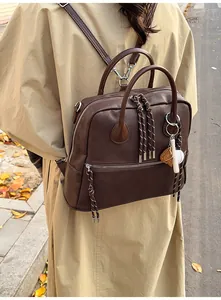 Dettaglio dello zaino vintage in pelle marrone con ciondolo da baseball e tira zip intrecciati