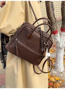 Dettaglio dello zaino vintage in pelle marrone con ciondolo da baseball e tirazip a corda