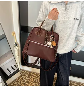 Dettaglio dello zaino bordeaux in pelle con ciondoli da baseball e trama litchi