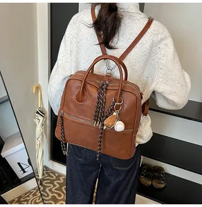 Dettaglio zaino vintage in pelle marrone con nappa in corda e ciondolo da baseball