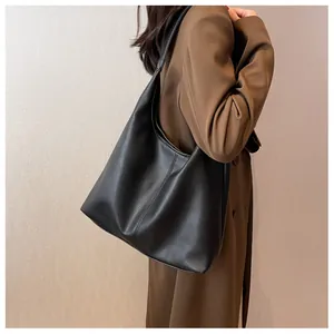 Close-up of black hobo tote bag with lychee texture worn by a model in a trench coat
