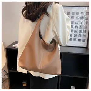 Detail of a large brown pebbled leather tote bag with wide shoulder strap on a model