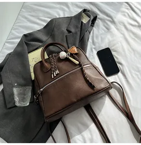 Dettaglio di uno zaino vintage marrone scuro su un blazer grigio con ciondoli