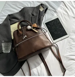 Dettaglio zaino vintage in pelle marrone con ciondolo da baseball su lenzuolo bianco