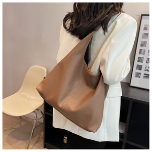 Close-up of large camel lychee grain leather bucket bag worn by model in white blazer
