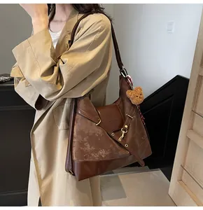 Detail view of large brown suede tote bag with leather patchwork and bear keychain charm