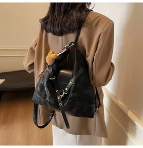 Detail of black leather tote bag with brown bear charm and decorative scarf on shoulder