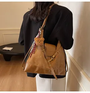 Detail of tan tote bag with bear charm and silk scarf shown on model shoulder