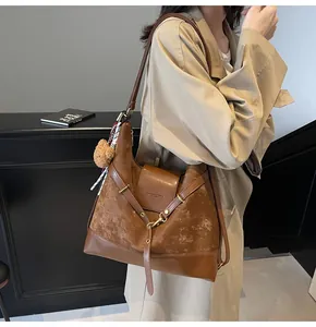 Detailed view of brown tote bag with suede stitching, metal hardware and plush bear charm
