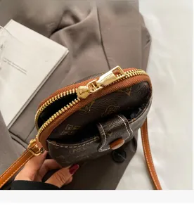 Detail view of smooth golden zipper and monogram pattern on brown crossbody phone bag