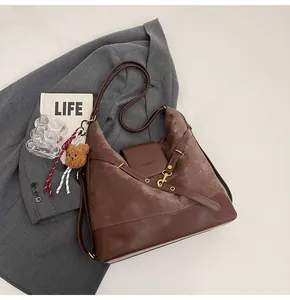 Detail of a deep brown faux leather and matte suede tote bag with a plush bear charm