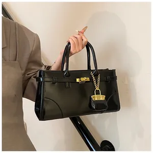 Detailaufnahme der glänzenden schwarzen Ledertasche mit goldener Schließe und Anhänger