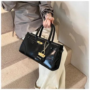 Detail einer glänzenden schwarzen Lackledertasche mit goldenem Schloss und Kettenelement