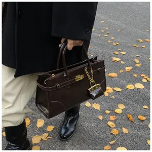 Detail einer dunkelbraunen Ledertasche mit Goldschnalle auf einer herbstlichen Straße