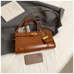 Detail einer braunen Ledertasche mit goldenem Drehverschluss und Mini-Umschlaganhänger