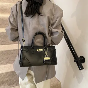 Schwarze glänzende Tragetasche mit goldenen Beschlägen und Gurt am Model