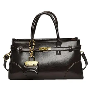 Dunkelbraune Hochglanz-Ledertasche mit goldenem Schloss und Schultergurt auf weißem Grund