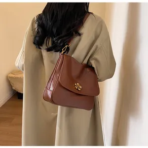 Brown leather crossbody bag with gold flower buckle shown on khaki trench coat