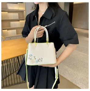 Close-up of floral embroidery on off-white tote bag with green trim and gold V hardware