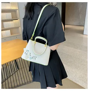 Detail of white embroidered tote bag with green piping and floral pattern on strap