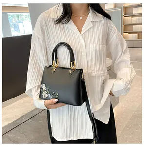Detailed embroidery on a black leather tote bag with elegant gold V-shaped hardware