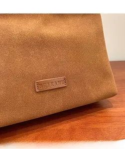 Detail of caramel brown suede handbag showing the brand logo and grainy leather texture