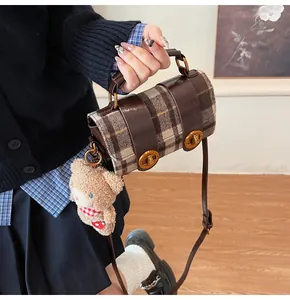 Dettaglio borsa a quadri vintage con finiture in pelle marrone e ciondolo a orsetto