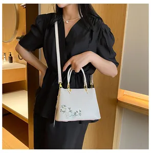Close-up of floral embroidery detail and gold hardware on white urban tote bag