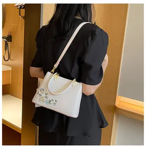 Close-up of elegant floral embroidery on a white leather tote bag with gold metal hardware