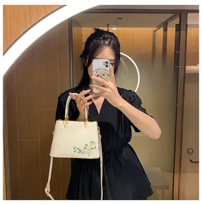 Detail of floral embroidery and gold hardware on white tote bag with adjustable strap