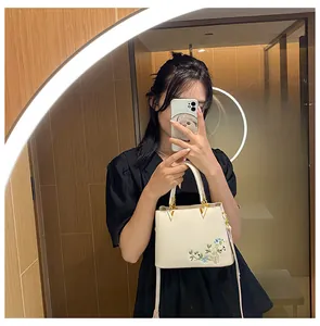 Detailed view of floral embroidery on a cream faux leather tote bag with gold hardware
