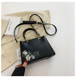Detailed embroidery of colorful flowers on a black faux leather crossbody tote bag